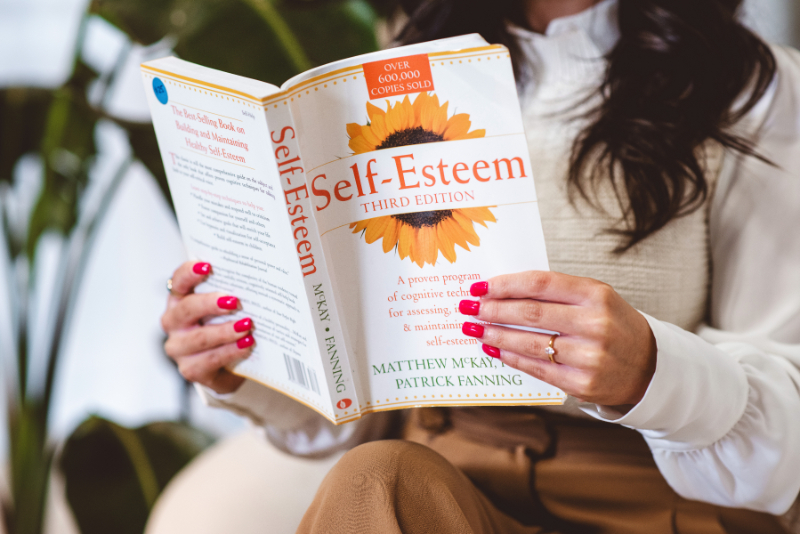 Person reading self-esteem book, reflecting on setting boundaries in relationships and building confidence and emotional awareness