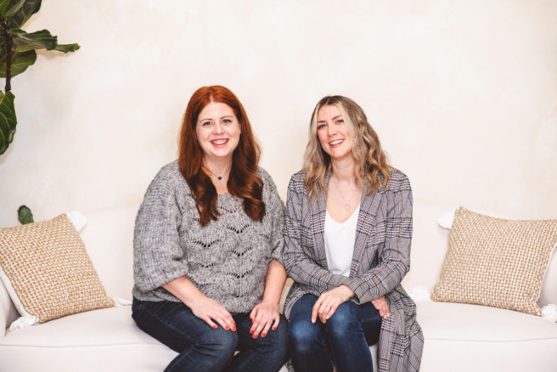 Two women sitting together on a couch, smiling warmly in a calm and welcoming space