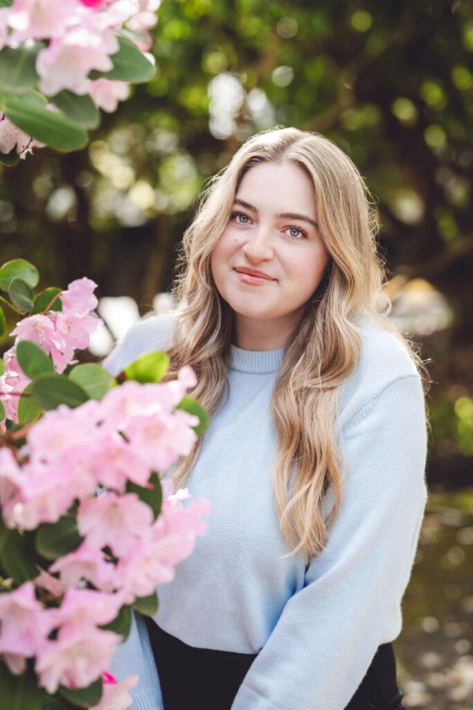 Smiling woman outdoors near pink flowers, relaxed expression in a calm natural setting