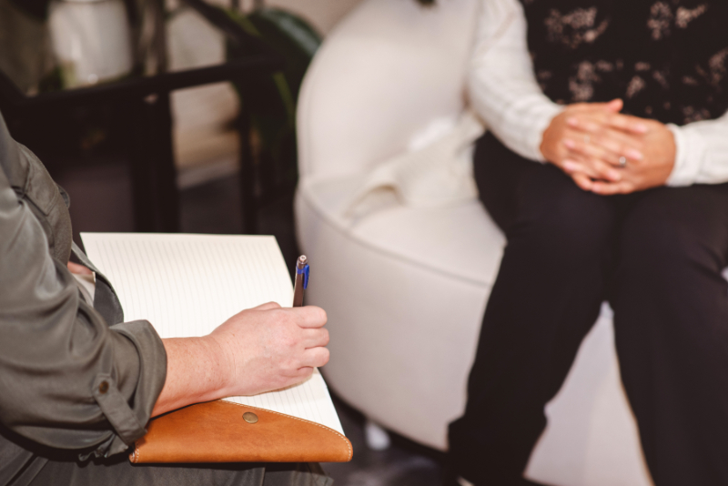 Therapist taking notes while client sits in chair, calm counselling session focused on support and listening
