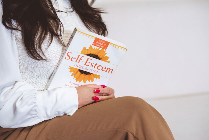 Person holding self-esteem book, supporting body image and mental health growth and self-reflection