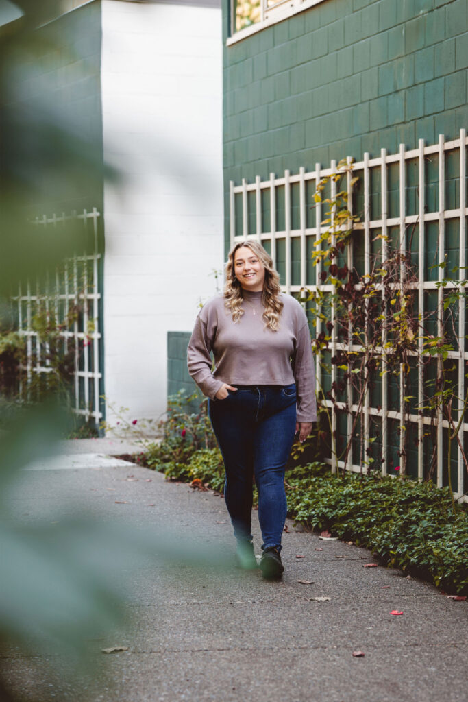 Woman walking outdoors in a calm setting with greenery and soft natural light.