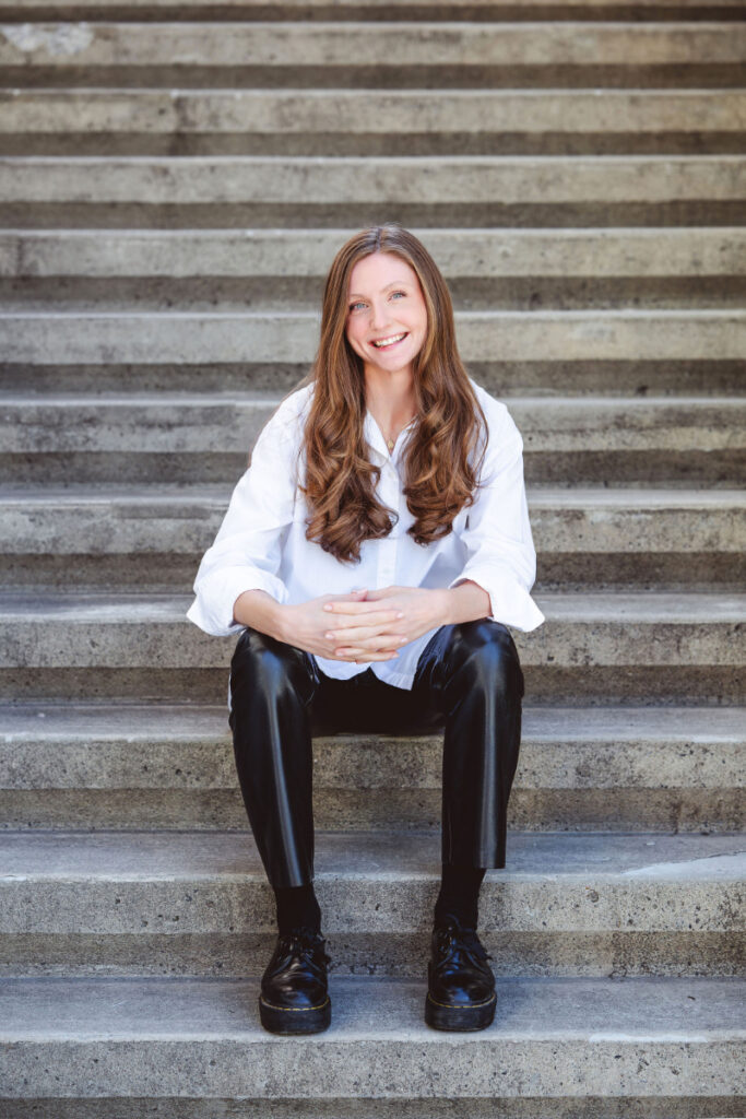 A smiling woman with long brown hair sits on steps, representing support when dealing with an eating disorder.